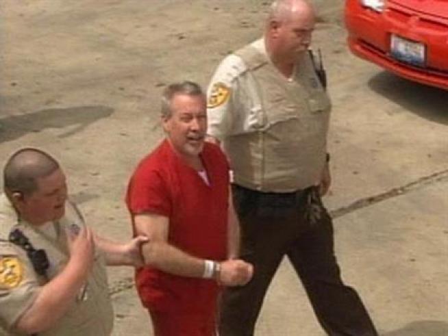 A shackled Drew Peterson is escorted by armed officers into the Will County Courthouse.