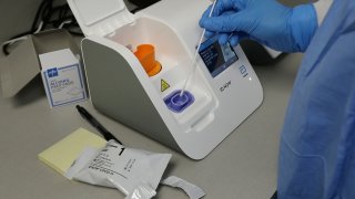 In this April 10, 2020, file frame grab from video, a lab technician dips a sample into the Abbott Laboratories ID Now testing machine at the Detroit Health Center in Detroit.