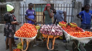 In this April 13, 2020, file photo, a woman buys tomatoes and onions from street sellers in Lagos, Nigeria. Lockdowns in Africa limiting the movement of people in an attempt to slow the spread of the coronavirus are threatening to choke off supplies of what the continent needs the most: Food.