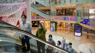 In this April 15, 2020 photo, people wear facemasks to protect against the spread of the new coronavirus cleans as they ride an escalator at a shopping mall in Beijing. China has reported its biggest economic decline since the 1970s as it fought the coronavirus in the first quarter of the year.