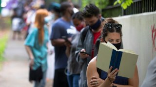 Kelsey Luker reads as she waits in line to vote, Tuesday, June 9, 2020, in Atlanta. Luker said she had been in line for almost two hours.