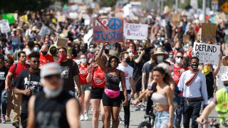 Desiree Wallace, center, of Denver, holds a placard while moving with fellow demonstrators down Sable Boulevard during a rally and march over the death of 23-year-old Elijah McClain, Saturday, June 27, 2020, in Aurora, Colo. McClain died in late August 2019 after he was stopped while walking to his apartment by three Aurora Police Department officers.