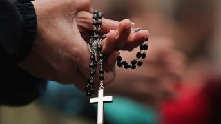 A pair of hands holds a rosary, with a cross hanging from it.