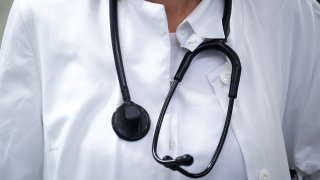 A doctor in a white lab coat wears a stethoscope around their neck