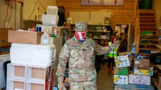 A member of the Indiana National Guard wearing a balaclava supports volunteer workers in distributing food at Pantry 279 to help those experiencing food insecurity during the COVID-19/Coronavirus stay-at-home order. Hoosiers have been ordered to only travel for essential needs.