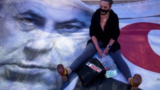 A woman sits on a placard showing Israeli Prime Minister Benjamin Netanyahu