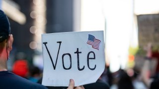 In this June 14, 2020, file photo, a protester holds a sign that says "Vote" with an American Flag as they march through the streets of New York City.