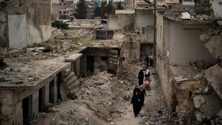 In this Thursday, March 12, 2020 photo, women walk in a neighborhood heavily damaged by airstrikes in Idlib, Syria.