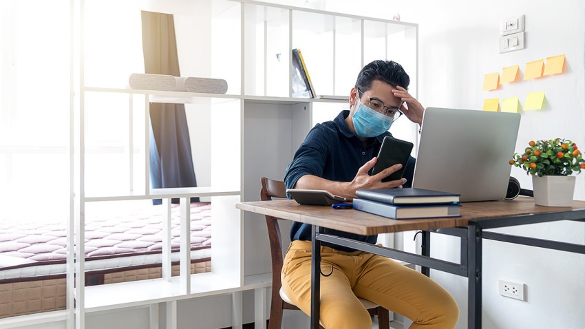 Concentrated Businessman ware mask sitting on working table and looking at Smart phone. Man working from home during corona virus quarantine.