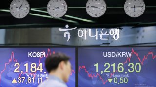 In this June 4, 2020, file photo, a currency trader walks by the screens showing the Korea Composite Stock Price Index (KOSPI), left, and the foreign exchange rate between U.S. dollar and South Korean won at the foreign exchange dealing room in Seoul, South Korea.