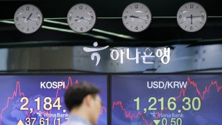 In this June 4, 2020, file photo, a currency trader walks by the screens showing the Korea Composite Stock Price Index (KOSPI), left, and the foreign exchange rate between U.S. dollar and South Korean won at the foreign exchange dealing room in Seoul, South Korea.
