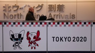 FILE – A traveler walks past a Tokyo 2020 banner in the arrivals area at Narita International Airport, east of Tokyo, Dec. 23, 2019.