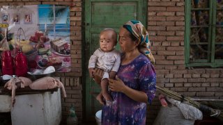 In this Sept. 12, 2016, file photo, a Uyghur woman holds a child in her home as they prepare food during the Corban Festival in Turpan County, in the far western Xinjiang province, China.