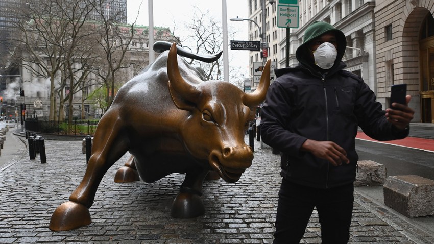In this file photo, a man wearing a face mask takes a selfie at the Charging Bull statue on March 23, 2020, outside the New York Stock Exchange in Manhattan.