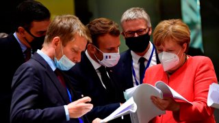 German Chancellor Angela Merkel, right, speaks with French President Emmanuel Macron, center, during a round table meeting at an EU summit in Brussels, Monday, July 20, 2020.
