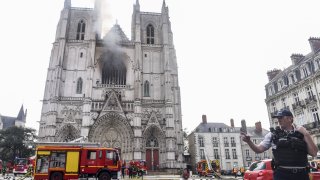 A French Police officer gestures as firefighters are at work to put out a fire at the Saint-Pierre-et-Saint-Paul cathedral in Nantes, western France, on July 18, 2020. - The major fire that broke out on July 18, 2020 inside the cathedral in the western French city of Nantes has now been contained, emergency services said. "It is a major fire," the emergency operations centre said, adding that crews were alerted just before 08:00 am (0600 GMT) and that 60 firefighters had been dispatched.