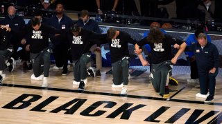 Members of the Milwaukee Bucks join arms as they kneel during the national anthem before an NBA basketball first round playoff game against the Orlando Magic Saturday, Aug. 29, 2020, in Lake Buena Vista, Fla.