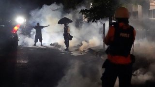 A protester holds his hands in the air after Portland police fired smoke into a crowd gathered in front of the Portland Police Bureau North Precinct early in the morning, Aug. 22, 2020, in Portland, Ore.