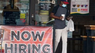 A customer wears a mask and looks at their cell phone as they carry their order past a now hiring sign at an eatery in Richardson, Texas, Wednesday, Sept. 2, 2020.