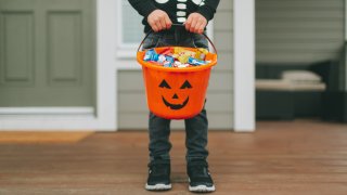 Low Section Of Boy With Sweet Food In Bucket Standing At Home During Halloween