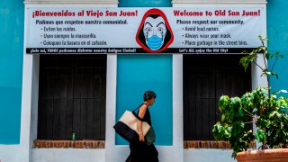 A woman walks pass by a banner urging visitors to wear face masks in San Juan, Puerto Rico