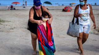 Wearing a mask as a precaution against the spread of the new coronavirus, a woman towels off a child at a beach in Havana, Cuba, Sunday, Oct. 11, 2020.