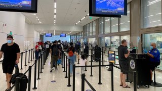 A Transportation Security Administration (TSA) agent wearing a protective face mask and sitting behind a barrier checks the identification of a traveler at the airport security screening center in Salt Lake City, Utah, Oct. 8, 2020.