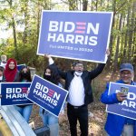 Gwinnett county voters including Menar Hague (C) wave Biden-Harris campaign signs at the entrance to Lucky Shoals Park polling station on November 3, 2020 in Norcross, Georgia.