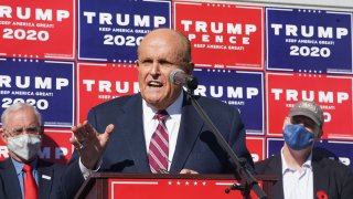 Attorney for the President, Rudy Giuliani, speaks at a news conference with Trump election posters in the background.