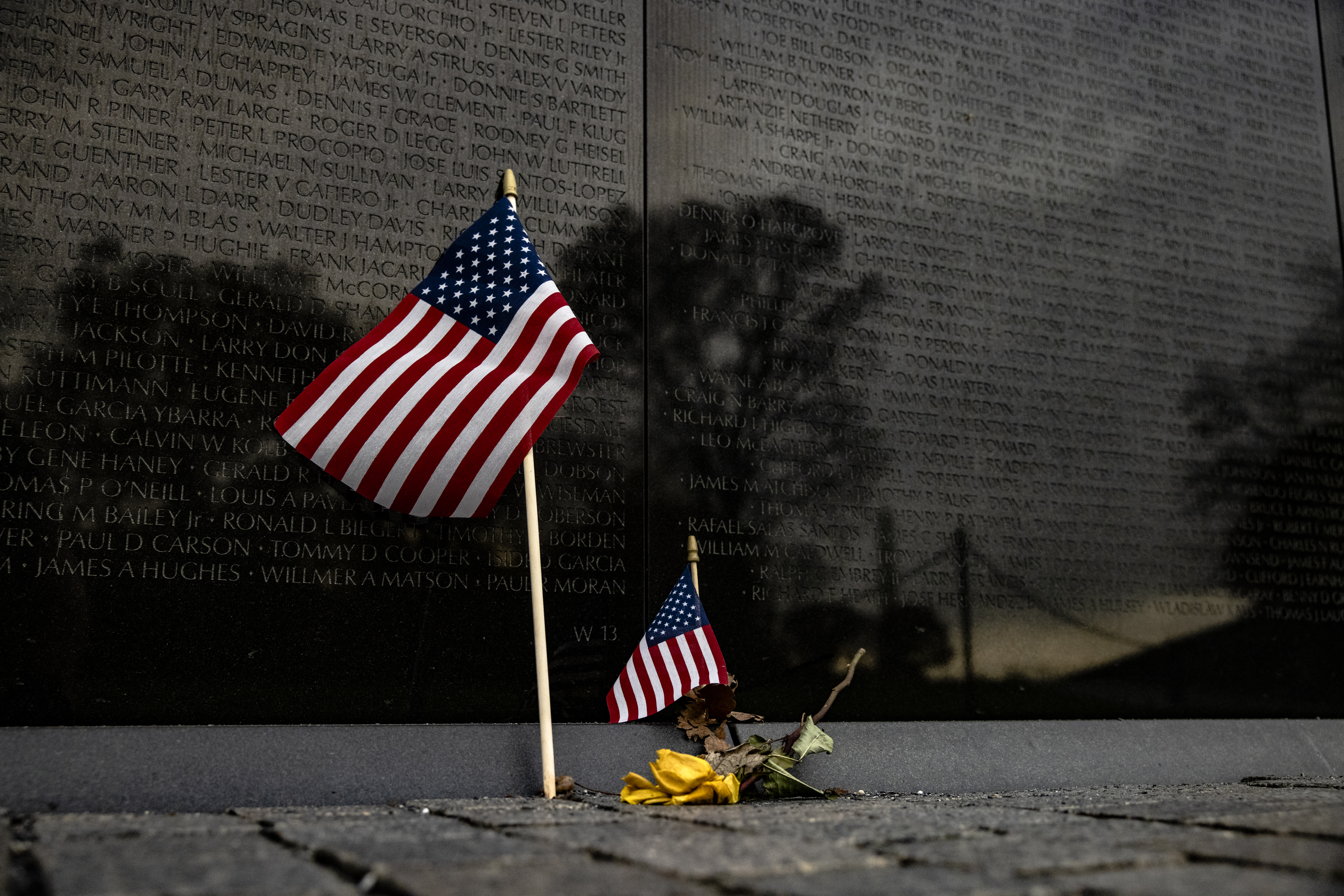 WASHINGTON, DC – NOVEMBER 11: A flower and two American flags are left at the base of the Vietnam Veterans Memorial Wall on Veterans Day on November 11, 2020 in Washington, DC. Veterans Day is when Americans honor those who served the country in the Armed Forces. The Vietnam Veterans Memorial Wall contains 58,320 names of those who gave their lives during the conflict in Vietnam. It was designed by Maya Lin and was completed in 1982. (Photo by Samuel Corum/Getty Images)