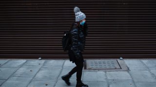 A woman wearing a face mask walks past a temporarily-closed store