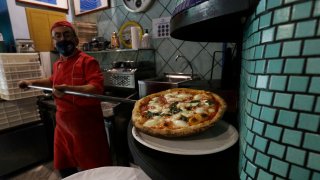 Eugenio Iorio wears a face mask to curb the spread of COVID-19 as he bakes a pizza at a restaurant in Naples, Italy