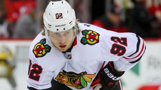 Blackhawks forward Alex Nylander, wearing a white Blackhawks jersey with a white helmet, awaits a faceoff against the New Jersey Devils