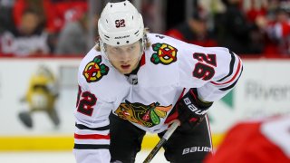 Blackhawks forward Alex Nylander, wearing a white Blackhawks jersey with a white helmet, awaits a faceoff against the New Jersey Devils