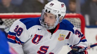 Landon Slaggert, wearing a white Team USA jersey with blue and red lettering, skates past the goal during a game in the Four Nations tournament