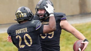 Two Northwestern University football players, wearing black uniforms with black helmets and gold trim throughout, celebrate a touchdown against Illinois in the annual rivalry game between the schools