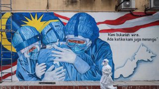A health worker wearing a personal protective equipment walks past an alley with a mural illustrating medical frontliners outside Clinic Ajwa in Shah Alam, Malaysia.