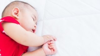 Portrait of an Asian newborn baby sleeping on a white bed at home.