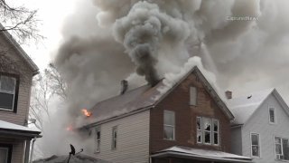 A two and a half story residence burns in Chicago's Englewood neighborhood, with smoke pouring from the roof and flames appearing through holes in the roof and at least one window of the structure