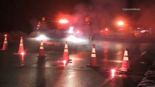Lake County sheriff's deputies examine a shooting scene in Volo; pictured are two police cars, with red lights flashing and fog rising from the street, along with red road flares and orange traffic cones