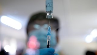 Blurry photo of a health care worker with a needle in a vial of the coronavirus vaccine.