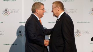 FILE - In this Saturday, May 4, 2019 file photo, International Olympic Committee President Thomas Bach, left, shakes hands with Australian Olympic Committee (AOC) President John Coates at the AOC annual general meeting in Sydney, Australia. The Australian Olympic bid is on a fast-track to host the 2032 Olympics Wednesday Feb. 24, 2021, after the International Olympic Committee executive board gave Queensland “preferred bidder” status, 11 years ahead of the games.