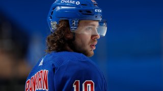 Rangers star Artemi Panarin is shown wearing a blue helmet with a clear visor, a blue Rangers jersey with red lettering and numbers