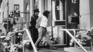 In this Oct. 24, 1981, file photo, David J. Gilbert, right, is escorted by police into the Village Hall in Nyack, N.Y., for a hearing on felony murder charges stemming from the Oct. 20, 1981, Brink's armored car robbery at a mall in Nanuet, N.Y., and a subsequent shootout with Nyack police that left three people dead. Now 76 years old, Gilbert, is still imprisoned in New York state after nearly four decades. Gilbert's son, San Francisco chief District Attorney Chesa Boudin, and other allies are lobbying for clemency for Gilbert as coronavirus cases rise among prison inmates.
