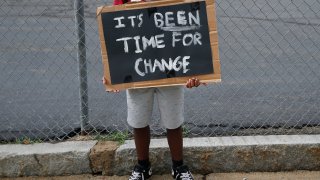Dewayne Henry, 14, holds a sign as he protests outside of Mystic Valley Regional Charter School in Malden, MA