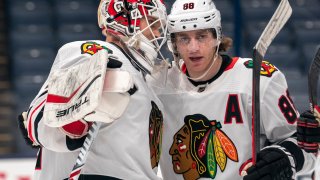 Kevin Lankinen and Patrick Kane, both wearing white Blackhawks jerseys, congratulate one another on a win over the Blue Jackets