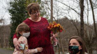 Margaux Irvine (L) the daughter of Chris Irvine, who passed from Covid-19 in January hugs her grandmother Sue, as her mother Carly (R) looks on near the James river in Lynchburg, Virginia on March 13, 2021