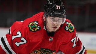 Blackhawks center Kirby Dach, wearing a red jersey and a black helmet, prepares for a face-off