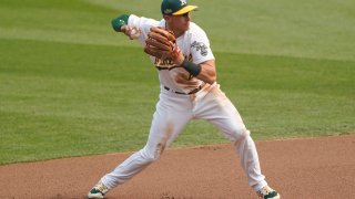 Jake Lamb, wearing a white jersey with green and gold lettering and a green Oakland Athletics cap, fields a ground ball