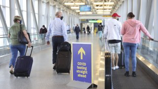 In this March 26, 2021, file photo, travelers wearing protective masks walk past a sign pointing towards a Covid-19 testing location in Terminal 5 at John F. Kennedy International Airport (JFK) in New York.